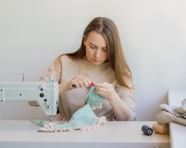 Young female tailor working on new garment at her workplace in studio