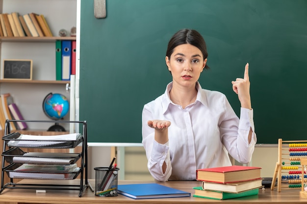 Giovane insegnante femminile seduta al tavolo con gli strumenti della scuola in classe