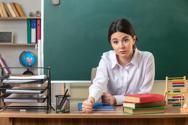 Giovane insegnante femminile seduta al tavolo con gli strumenti della scuola in classe