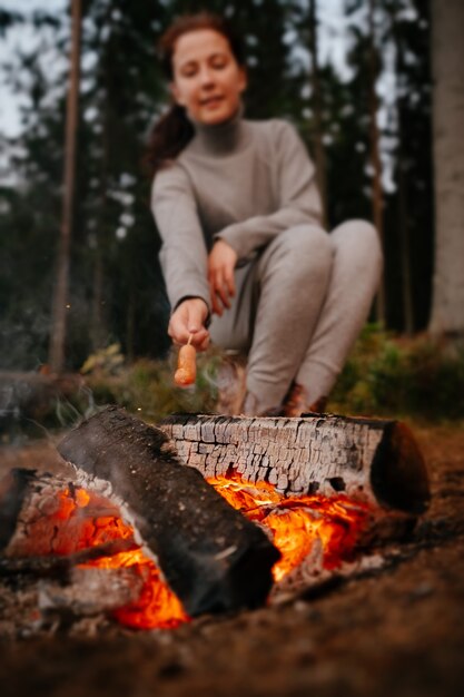 Young female tourist cooking barbecue sausages on a campfire selective focus on fire