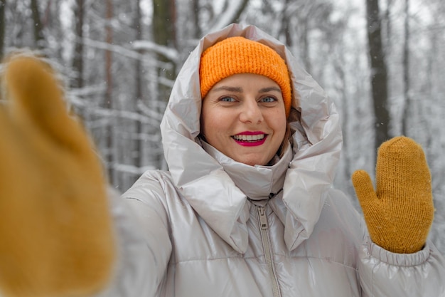 写真 暖かい服を着て黄色い手袋をかぶった若い女性観光客が山でハイキングしている冬の都市でセルフィーを撮っています