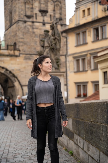 Photo young female tourist walking on the charles bridge in prague wearing dark clothes on a cloudy day