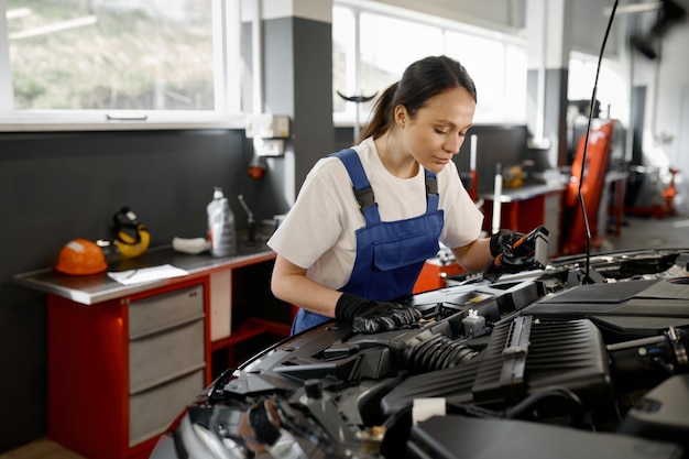 Young female tradesperson mechanic working on car engine using professional tools in auto repair garage