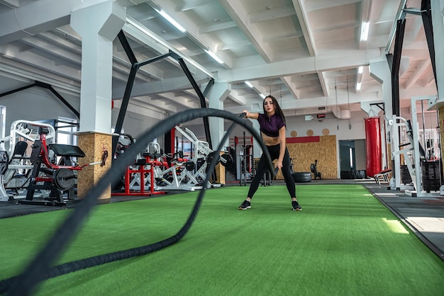 Тренировка молодой женщины-тренера с веревкой в спортзале