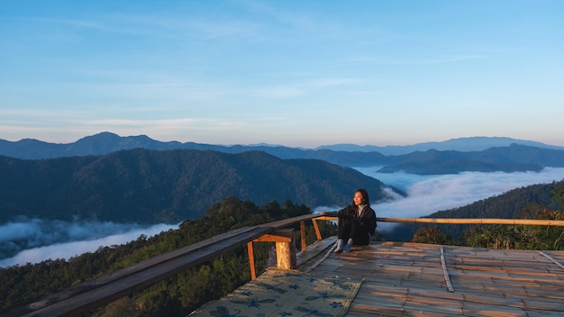 美しい山と霧の海を見ている木製のバルコニーに座っている若い女性旅行者