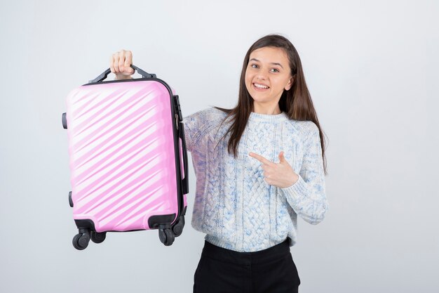 Turista femminile giovane viaggiatore con la valigia rosa in attesa di destinazione.