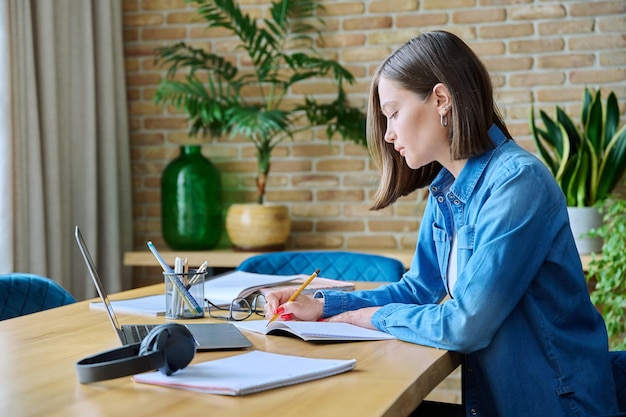 young female university student studying at home using laptop