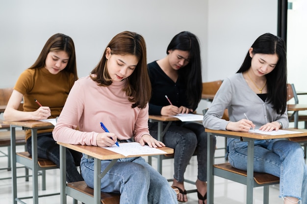 Young female university students concentrate on doing\
examination in classroom. girl students seriousely writes the\
exercise of the examinations in the classroom.