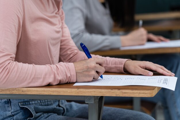 若い女子大生は教室での試験に集中しています。女子生徒は教室での試験問題を真剣に書いています。