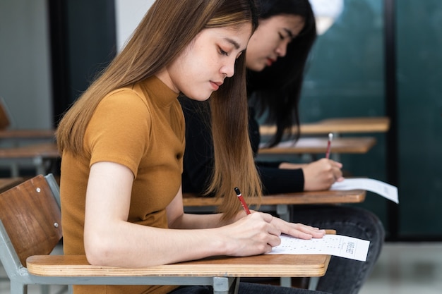 Young female university students concentrate on doing examination in classroom. Girl students seriousely writes the exercise of the examinations in the classroom.