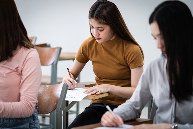 若い女子大生は教室での試験に集中しています。女子生徒は教室での試験問題を真剣に書いています。