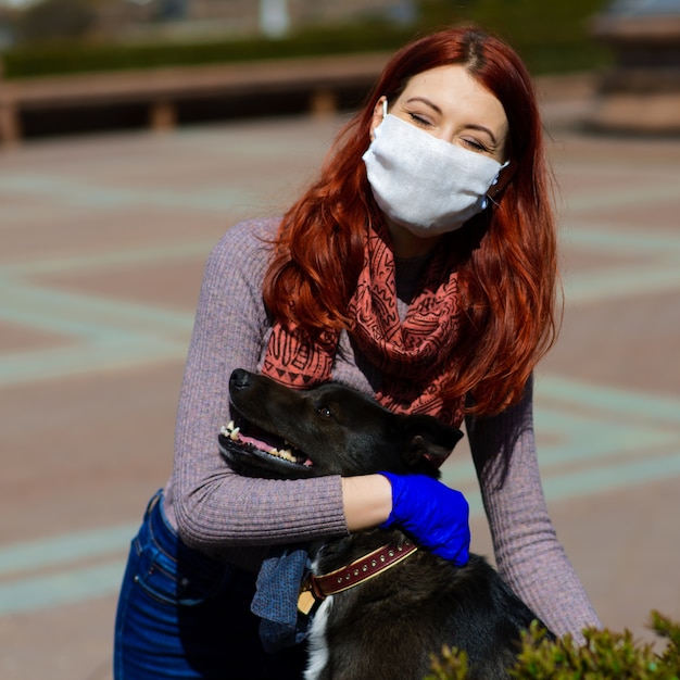 얼굴 마스크를 사용하는 젊은 여성은 그녀의 강아지와 함께 걷는 코로나 바이러스 확산 예방으로. 글로벌 COVID-19 대유행 컨셉 이미지.