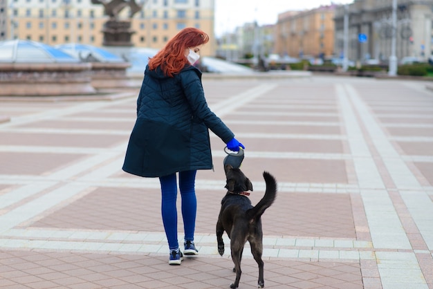 犬と一緒に歩くコロナウイルス拡散防止としてフェイスマスクを使用している若い女性