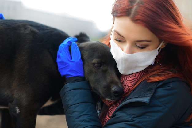 Young female using a face mask as a coronavirus spreading prevention walking with her dog