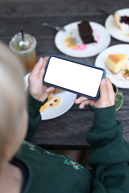 카페에서 쉬는 동안 맛있는 패스트리 사진을 찍는 스마트 폰을 사용하는 젊은 여성.