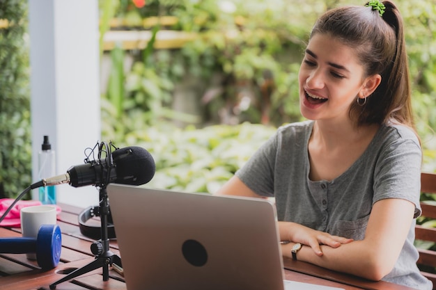 Young female vlogger with mic and dumbbells recording a video using laptop by talking and giving information and some tips and tricks on fitness to audience while sitting at home