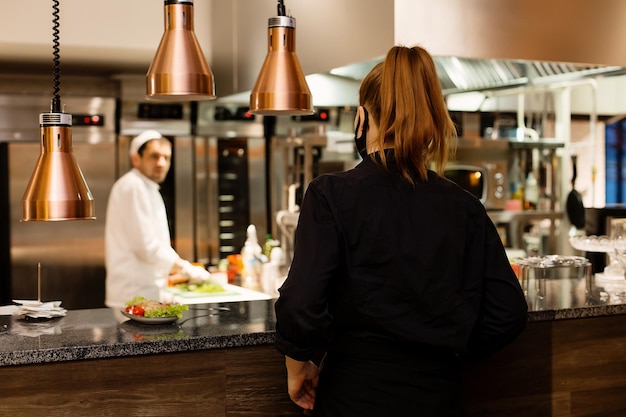 Young female waiter taking order of meal from restaurant kitchen