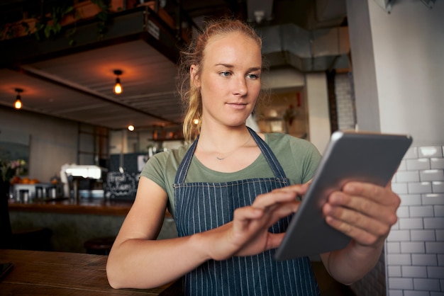デジタルタブレットを使ってオンライン注文をチェックするカフェの若い女性ウェイトレス