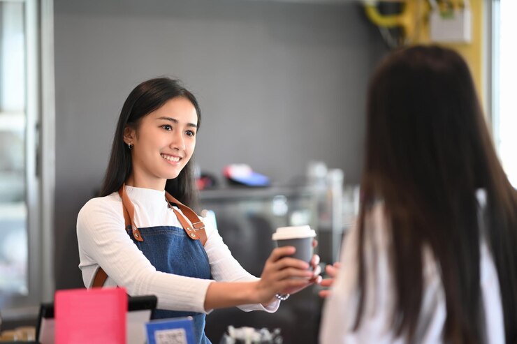 コーヒーショップで顧客に持ち帰り用のコーヒーカップを与える若い女性ウェイトレス。