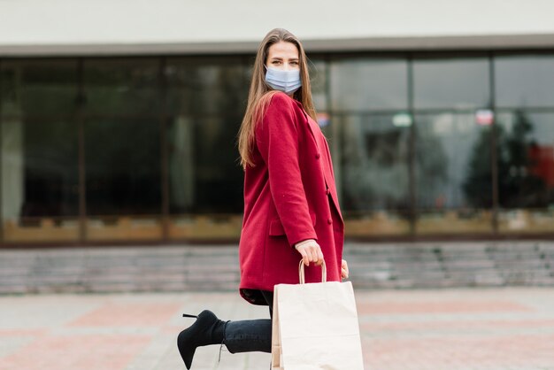 Young female wearing a mask for prevent virus with shopping bags on narrow street in Europe.