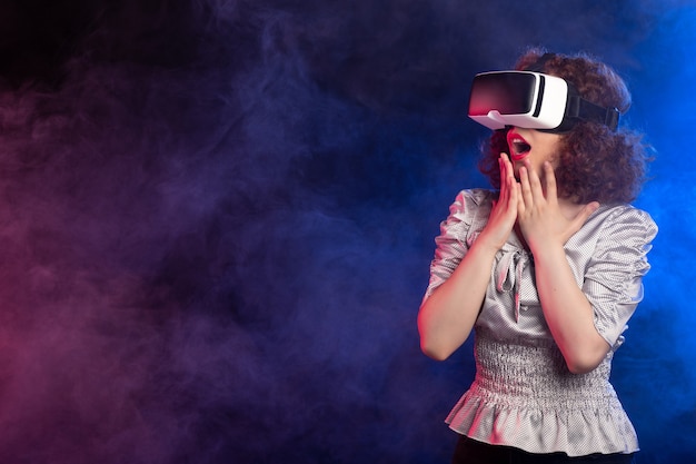 Young female wearing virtual reality headset on dark smoky  play video d