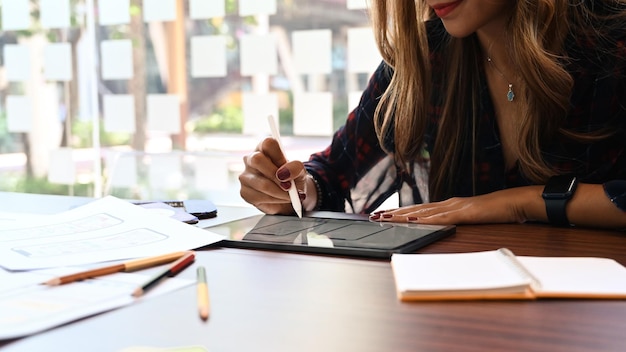 Young female web developer holding stylus pen and working on digital tablet at creative office