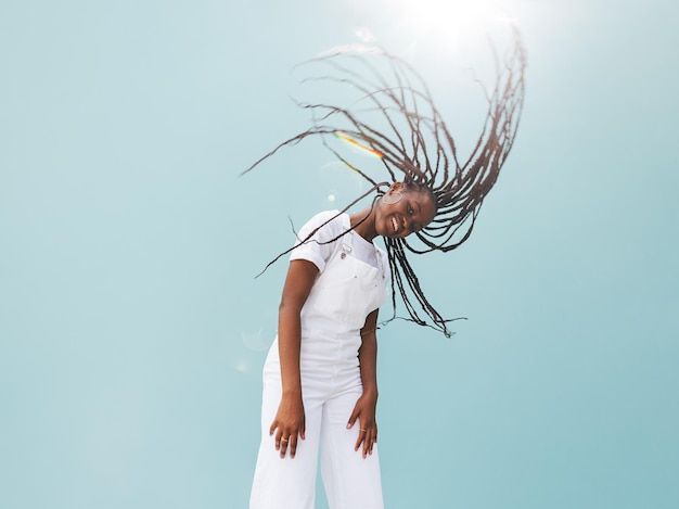 Young female in white casuals with long braids against blue wall