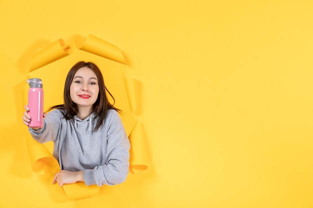 young female with bottle of water on torn yellow paper background athlete indoor gym