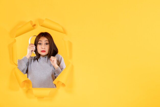 young female with headphones on a torn yellow paper background sound ultrasound audio