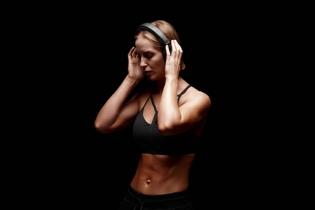 Young female with muscular body getting ready to workout and listen music in headphones