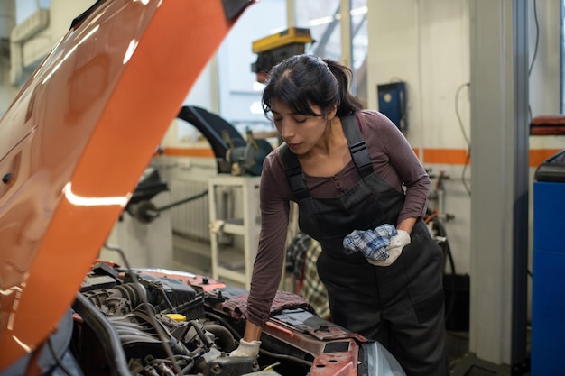 Young female worker of car maintenance service repairing vehicle