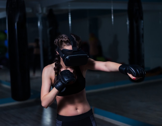 トレーニングでボクシンググローブを着用したVRメガネの若い戦闘機ボクサーフィットの女の子未来的なゲーム