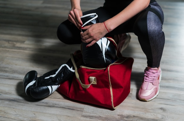 Young fighter boxer girl puting on boxing gloves before training. She has sport bag