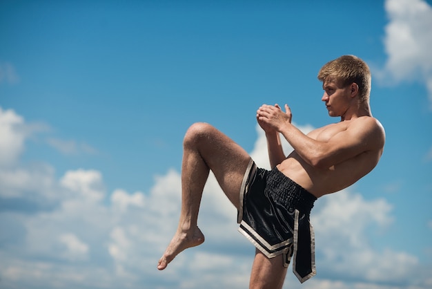 Young fighter kicking. Exercise in the open air. Knee kick