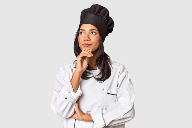 Foto giovane chef filippino con cappello da cucina in studio guardando di lato con dubbi e scetticismo