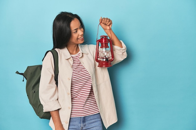 Young Filipina traveler holding a vintage lantern on blue backdrop