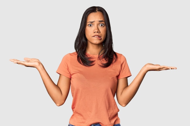 Young Filipina with long black hair in studio confused and doubtful shrugging shoulders