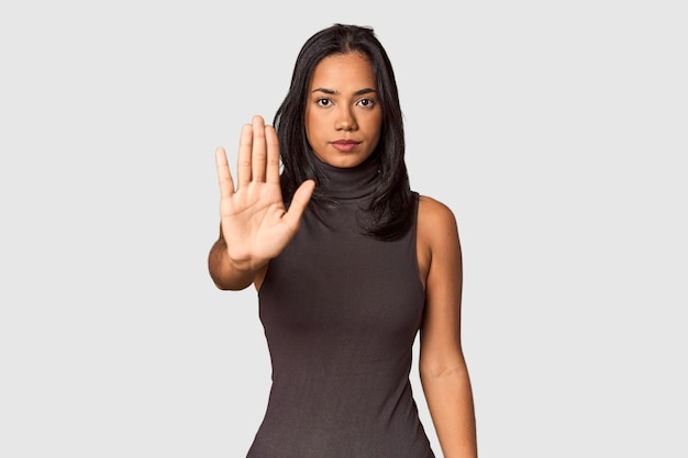 Молодая филиппинка с длинными черными волосами в студии стоит с вытянутой рукой, показывая знак остановки