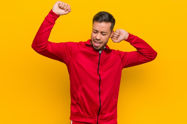 Young filipino fitness man celebrating a special day, jumps and raise arms with energy