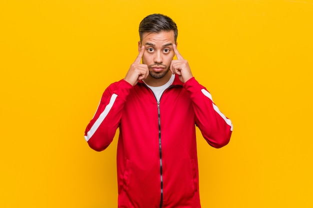 Young filipino fitness man focused on a task, keeping forefingers pointing head.