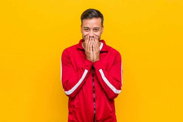 Young filipino fitness man laughing about something, covering mouth with hands.