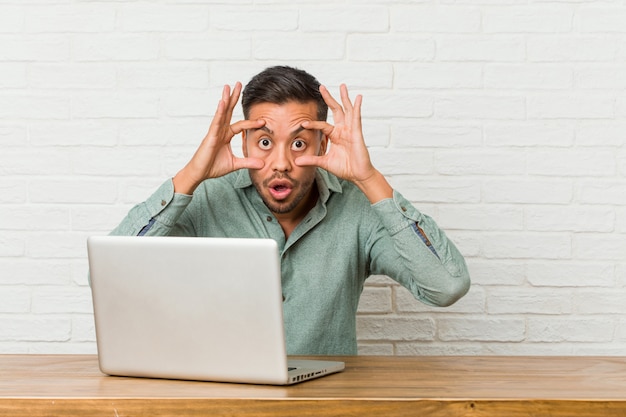 Young filipino man sitting working with his laptop keeping eyes opened to find a success opportunity.