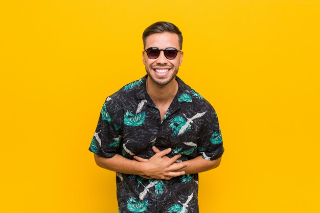 Photo young filipino man wearing summer clothes laughs happily and has fun keeping hands on stomach.