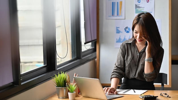 若い金融女性電話で呼び出して、ラップトップコンピューターを使用しています。