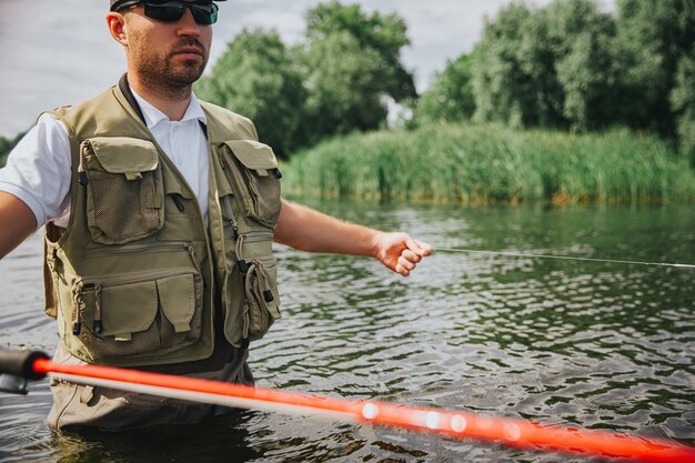 Giovane pescatore che pesca sul lago o sul fiume. tagliare la vista del ragazzo che tiene una lunga canna rossa e pesca da solo in mezzo al lago o al fiume. stai in acqua. bella giornata di sole.