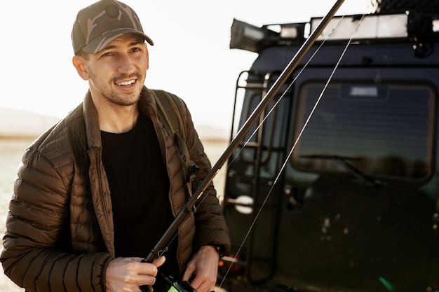 Young fisherman standing near his car and holding fishing equipment