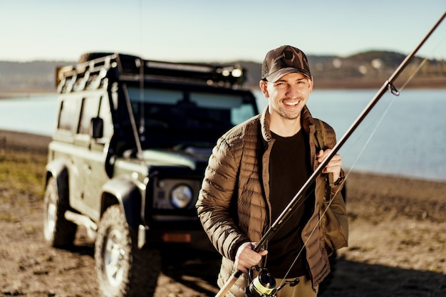 Young fisherman standing near his car and holding fishing equipment