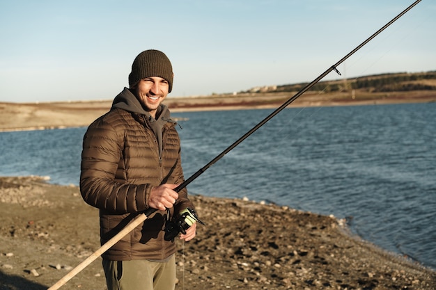 Giovane pescatore in piedi sulla riva del lago con canna da pesca