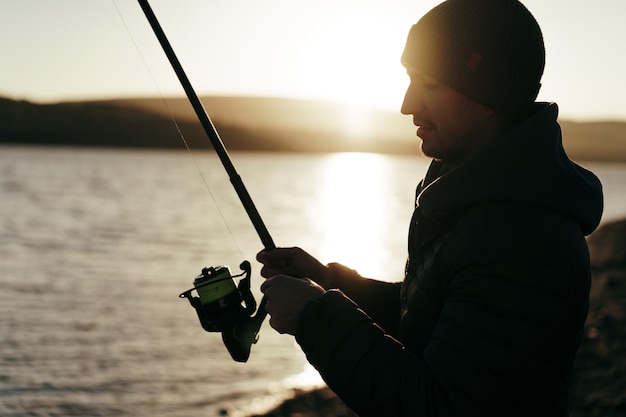 Foto giovane pescatore in piedi sulla riva del lago con canna da pesca