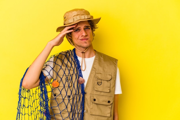 Photo young fisherman with makeup holding a net isolated on yellow background  being shocked, she has remembered important meeting.